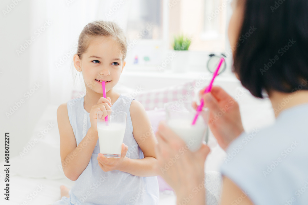 Mother and daughter sipping milk with straws, sharing a light-hearted moment. Mother and daughter sipping milk with straws, sharing a light-hearted moment.