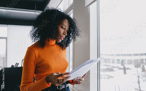 Photography A perceptive analyst in a bold orange sweater scrutinizes financial reports in a