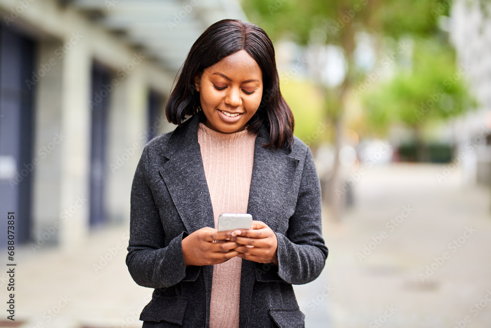 © Meeko Media - Young Black woman in formal wear looking at cell phone while walking outside