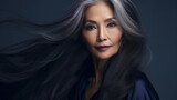 Smiling, elderly, chic Asian woman with gray long hair and perfect skin, on a dark blue background, banner.