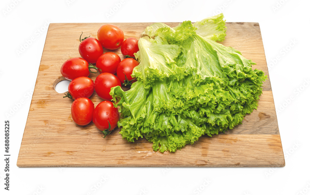 Bright red cherry tomatoes and green lettuce on a wooden board. Vegan food. Salad preparation.