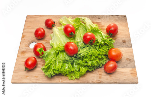 Bright red cherry tomatoes and green lettuce on a wooden board. Vegan food. Salad preparation.