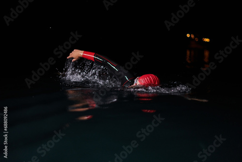 A determined professional triathlete undergoes rigorous night time training in cold waters, showcasing dedication and resilience in preparation for an upcoming triathlon swim competition © .shock