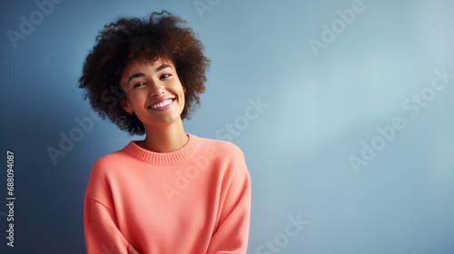 Young woman with curly hair smiling warmly, wearing a casual peach-colored shirt