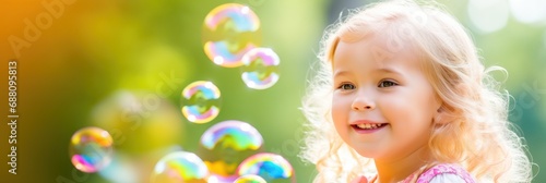 Happy little blonde girl playing with soap bubbles. Sunny day summer outdoor background. Wide panoramic banner.