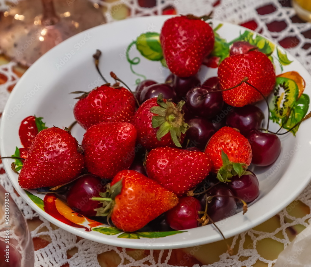 Strawberries and cherries in a white ceramic plate close-up on the background of a knitted tablecloth kitchen table Strawberries and cherries in a white ceramic plate close-up on the background of a knitted tablecloth kitchen table