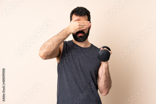 Caucasian sport man with beard making weightlifting over isolated background covering eyes by hands. Do not want to see something photo