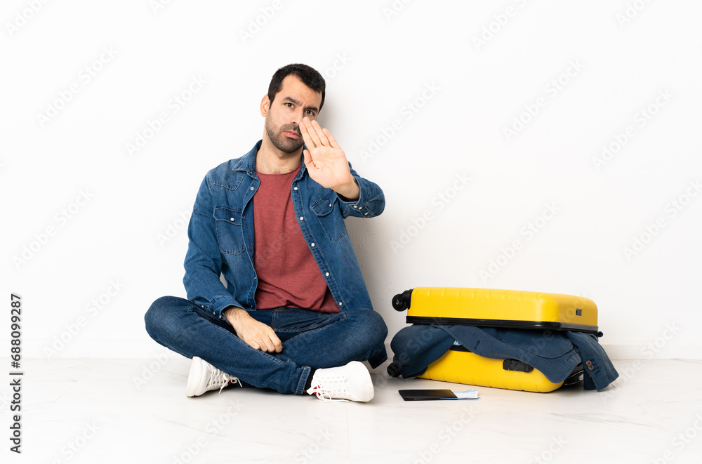 Caucasian handsome man with a suitcase full of clothes sitting on the floor at indoors making stop gesture Caucasian handsome man with a suitcase full of clothes sitting on the floor at indoors making stop gesture