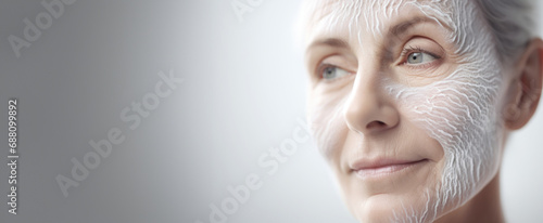 Against a pristine white background, a woman applies facial cream, engaging in a skincare ritual that celebrates the beauty of aging