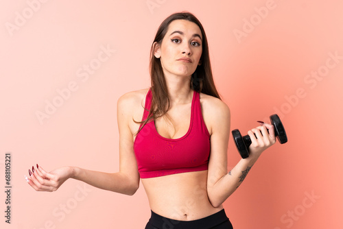 Young sport woman making weightlifting over isolated pink background making doubts gesture while lifting the shoulders © luismolinero