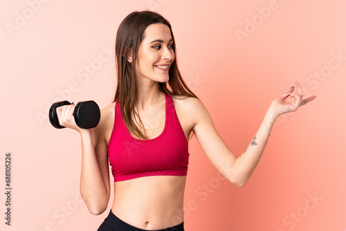 Young sport woman making weightlifting over isolated pink background pointing to the side to present a product