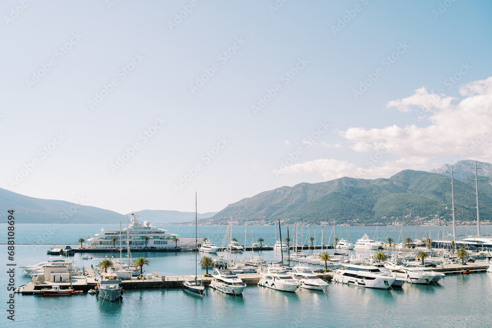 Expensive superyacht and motor yachts are moored to piers in the sea against the backdrop of mountains