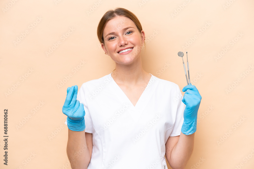 Dentist caucasian woman holding tools isolated on beige background making money gesture Dentist caucasian woman holding tools isolated on beige background making money gesture