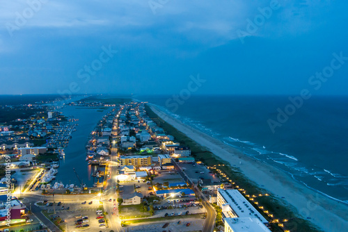 an aerial shot along the coastline of the Atlantic ocean with blue water, a sandy beach, hotels and condominiums and cars on the street at night with lights in Carolina Beach North Carolina USA