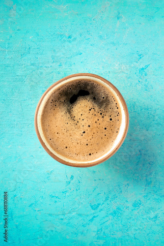 A cup of espresso coffee with froth, overhead flat lay shot on a teal background