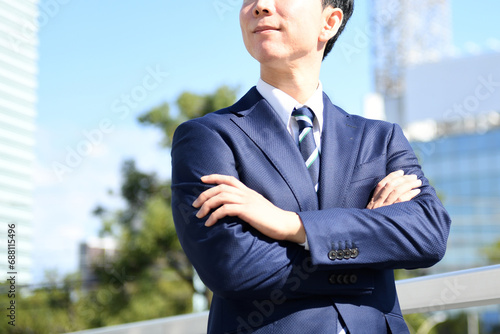 街中で腕組みをするスーツ姿のアジア人のビジネスマン