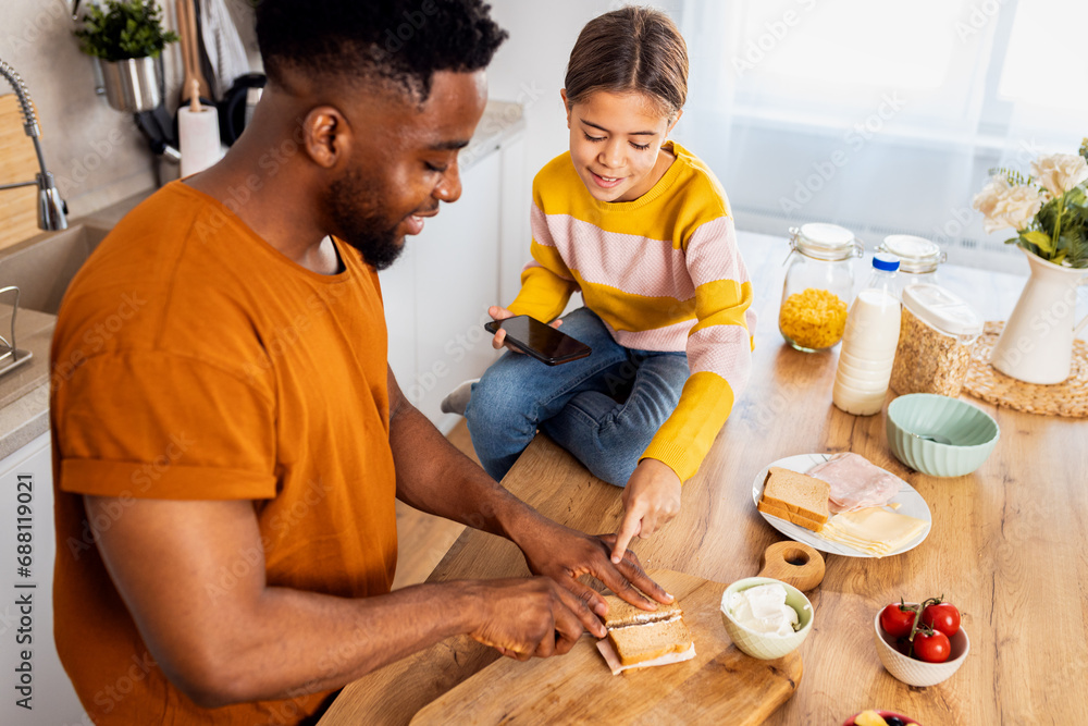Smiling young single father with his daughter preparing lunch for school in the kitchen at home. Smiling young single father with his daughter preparing lunch for school in the kitchen at home.