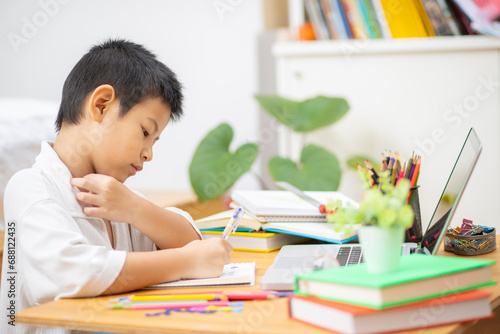 Asian Boy Doing homework with the intention. Child boy holding pencil writing, A boy drawing on white paper at the table,Elementary school and home schooling, Distance Education concept.