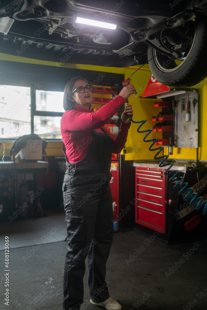 Mechanic working under the car at the repair garage. Portrait of a happy mechanic woman working on a car in an auto repair shop. Female mechanic working on car. Female Auto Mechanic
