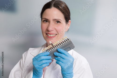 dentist's assistant / female dentist with medical gloves holds/shows shade guide to check veneer of teeth