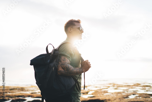 Happy man carrying backpack standing against ocean and sunlight photo
