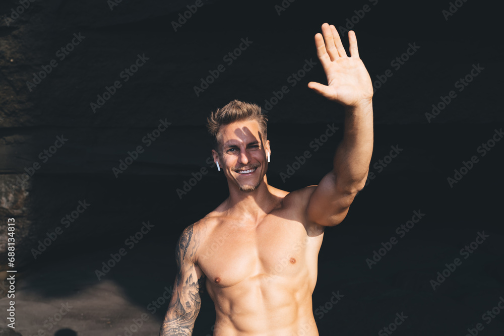 Fototapeta premium Cheerful young man with naked torso raising hand while blocking sunlight