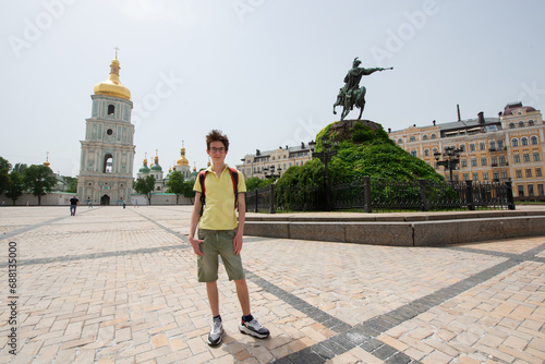 Young handsome teen boy looking at camera and happy smiling over Cathedral of St. Sophia of Kyiv and monument to Bohdan Khmelnitsky, summer city center