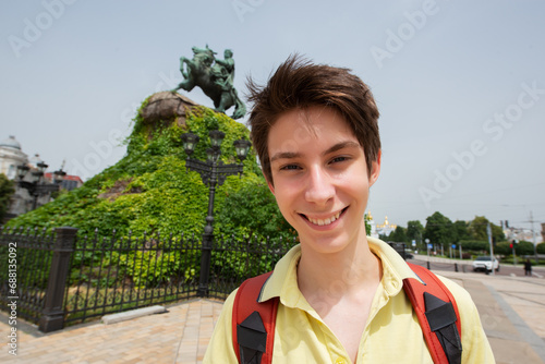 Young handsome teen boy looking at camera and happy smiling over monument to Bohdan Khmelnitsky, summer city center of Kyiv, Ukraine photo