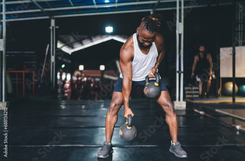 Fototapeta Naklejka Na Ścianę i Meble -  Strong black male athlete lifting kettlebells during workout in gym