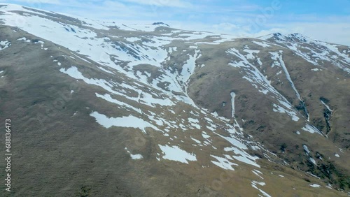 Aerial view of high mountains covered with snow with thawing on a sunny day against a blue sky. Deserted gray mountains in winter without grass with snowy peaks. Drone footage. Direct flight. Armenia