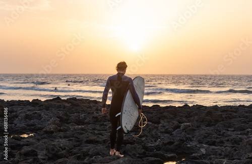 Rear View of Young Surfer going to the water Against a Orange Sunset Sky in Canary Island.Copy Space