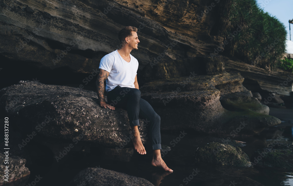 Happy man sitting on stone near water in rocky cliff