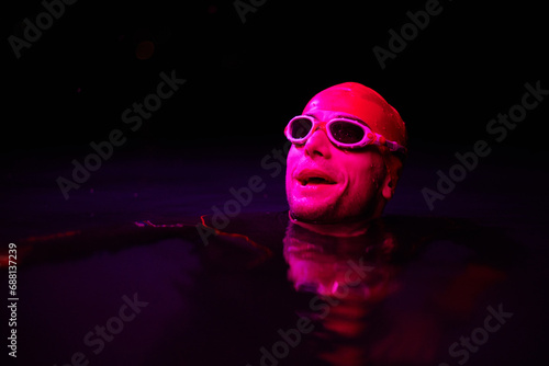 Authentic triathlete swimmer having a break during hard training on night neon gel light