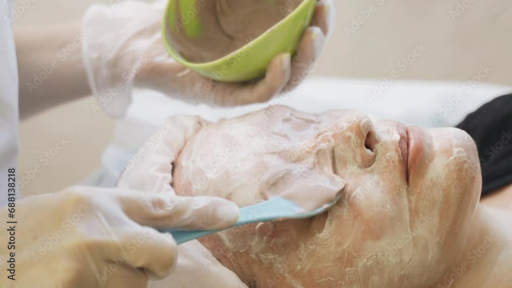A cosmetologist applies an alginate mask to a womans face with a cosmetic spatula. Close-up. A cosmetologist applies an alginate mask to a womans face with a cosmetic spatula. Close-up.
