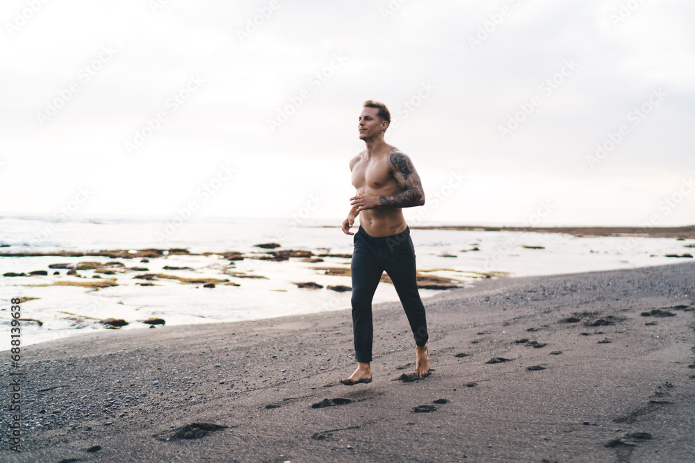 Fit shirtless man athlete jogging on wet beach near sea