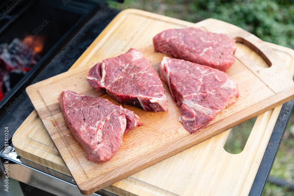 Four beef steaks lie on a cutting board next to the grill