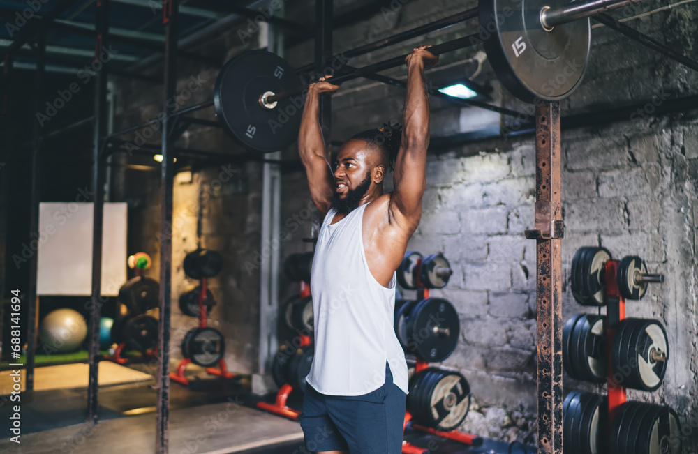 Strong black man exercising with barbell in gym