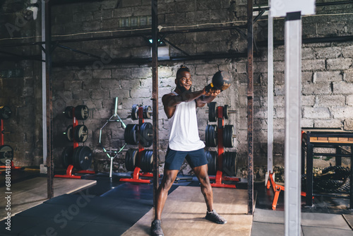 Muscular man standing and swinging heavy kettlebell in gym photo