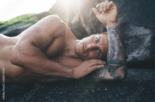 Shirtless man lying on sandy beach by rocky cliff