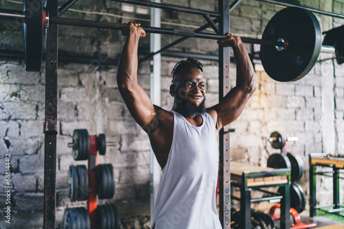 Muscular black sportsman lifting heavy barbell in gym photo