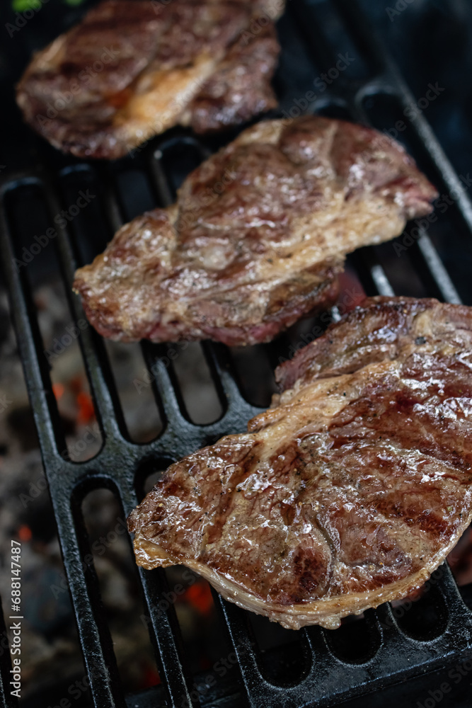 Three ribeye steaks are cooked on a charcoal grill on a cast iron grate Three ribeye steaks are cooked on a charcoal grill on a cast iron grate