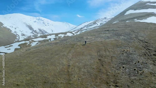 Aerial view of a man in the high mountains covered with snow with thawing on a sunny day against a sky. Deserted gray mountains in winter without grass with snowy peaks. Drone footage. Armenia