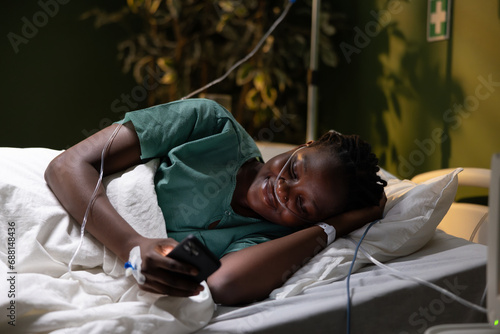Woman patient lies in the hospital bed, smiles, and holds a phone with an oxygen tube.