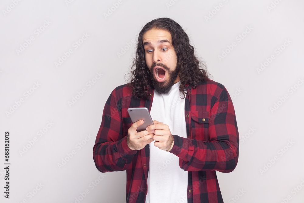 Portrait of addicted man feels impressed, reads shocking news, holds modern cell phone, connected to wifi, embarrassed with unexpected feedback. Indoor studio shot isolated on gray background. Portrait of addicted man feels impressed, reads shocking news, holds modern cell phone, connected to wifi, embarrassed with unexpected feedback. Indoor studio shot isolated on gray background.
