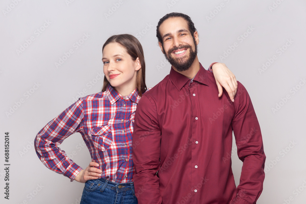 Portrait of smiling joyful cheerful woman and man standing together, wife hugging her husband, expressing positive emotions and happiness. Indoor studio shot isolated on gray background. Portrait of smiling joyful cheerful woman and man standing together, wife hugging her husband, expressing positive emotions and happiness. Indoor studio shot isolated on gray background.