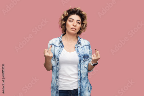 Portrait of rude impolite serious woman with curly hairstyle wearing blue shirt standing with middle fingers, arguing with somebody. Indoor studio shot isolated on pink background. photo