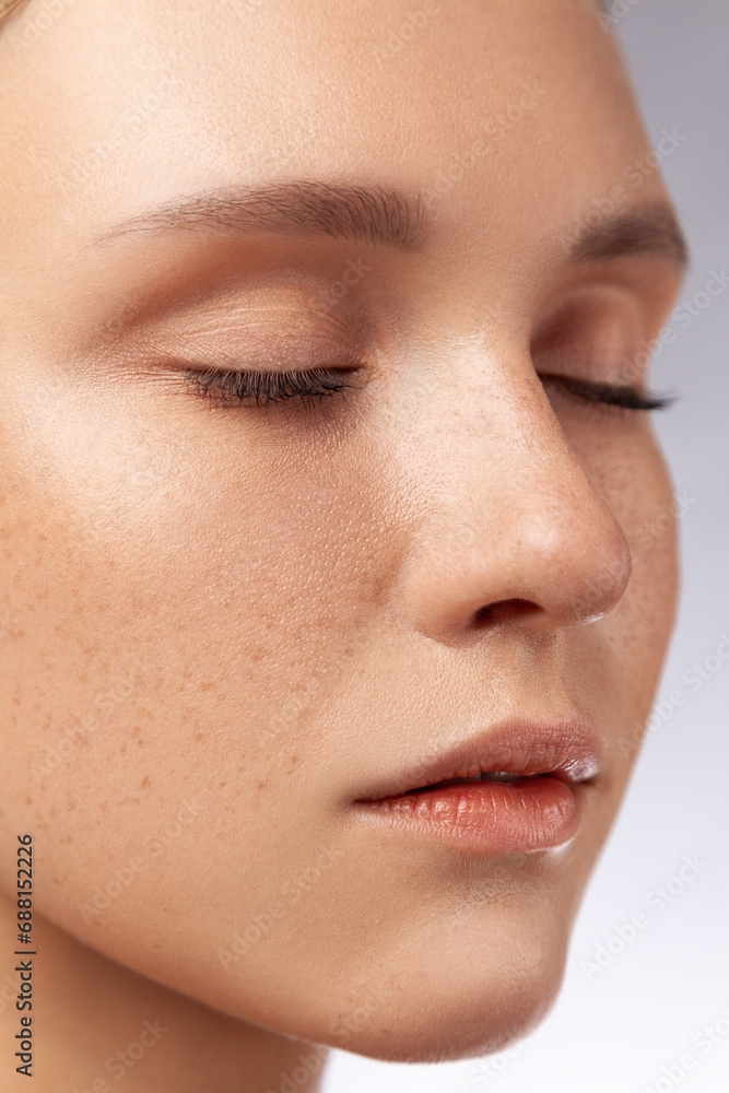 Fototapeta premium Closeup side view portrait of beautiful woman with perfect skin and natural makeup posing with closed eyes. Indoor studio shot isolated over gray background.