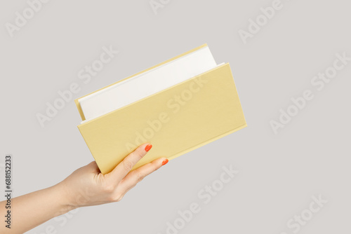 Closeup of woman hand holding open book or organizer. Indoor studio shot isolated on gray background.