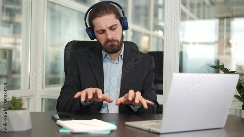 Emotional office worker listening music on wireless headphones while pretending to be member of band and playing on virtual instruments. Active caucasian businessman having fun in free time from work. photo