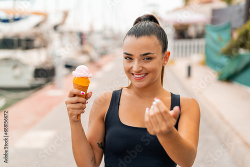 Young pretty woman with a cornet ice cream at outdoors inviting to come with hand. Happy that you came